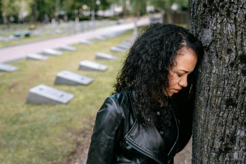 Woman in emotional distress leaning against a tree in cemetery