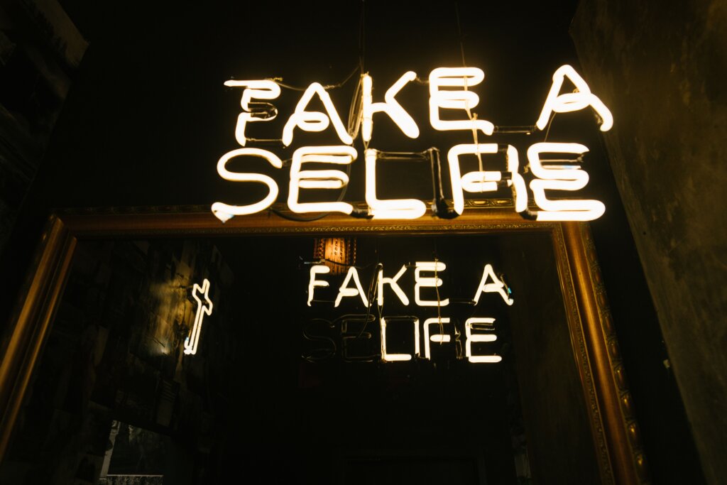 Neon sign stating, "Take a Selfie, Fake a Life"