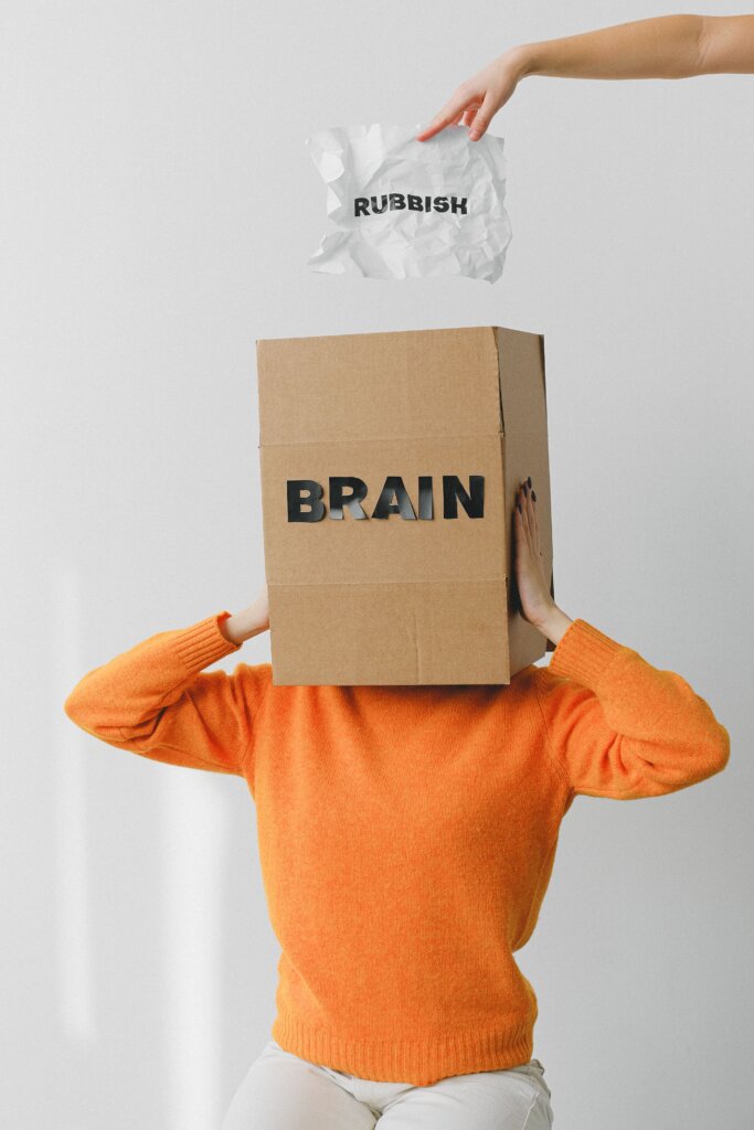 Woman with box over head labeled Brain and hand dropping paper with word rubbish into box