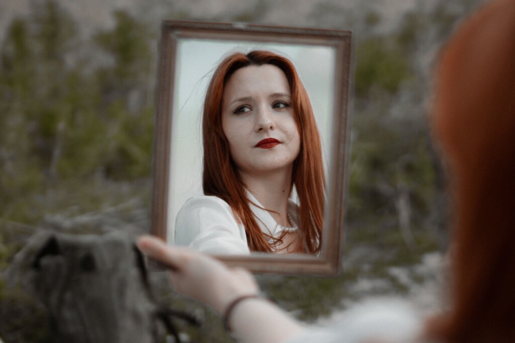 Reflection of girl with red hair in mirror she is holding with outstretched arm